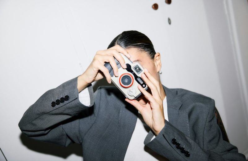 Person i grå kostym tar ett foto med en ljus kompaktkamera