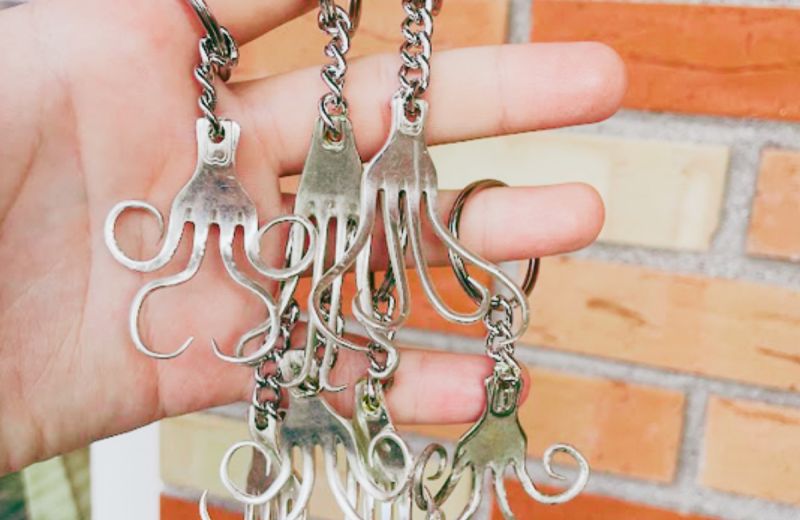Närbild på handgjorda smycken och nyckelringar skapade av återbrukade silverbestick mot en tegelvägg.