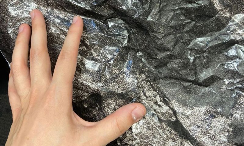 En hand vilar mot ett skrynkligt, silvrigt och mörkt material med en grov textur, som ska likna en sten.