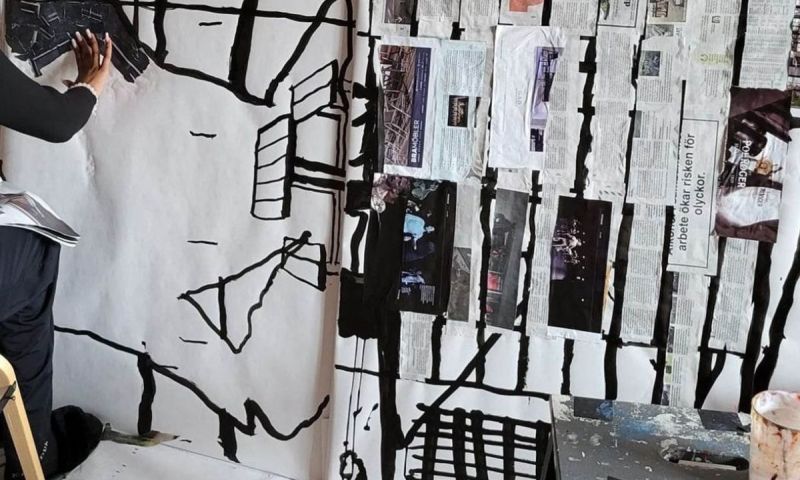 Person arbetar på ett stort blandteknik-konstverk med collage och svarta penseldrag.