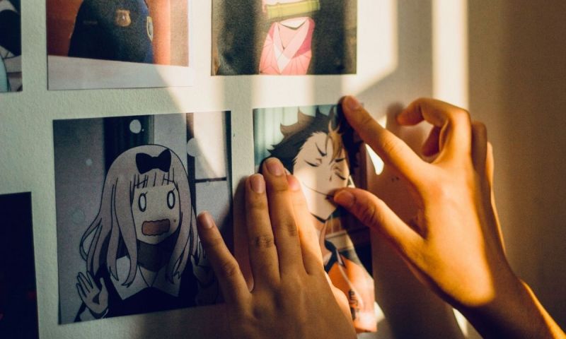 Två händer justerar utskrivna animebilder på en vägg i varmt solljus