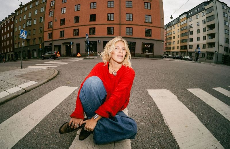 En ung kvinna sitter på ett övergångsställe och blickar in i kameran.