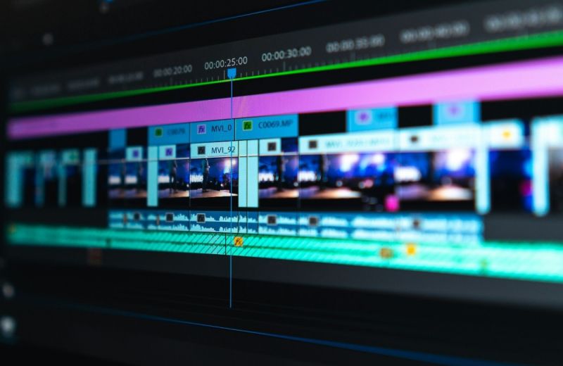 Närbild på en digital tidslinje under filmredigering med färgstarka videoklipp och ljudvågor i fokus.