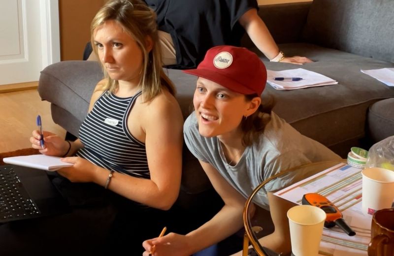 Två unga personer sitter på golvet och antecknar och lyssnar uppmärksamt under ett möte.