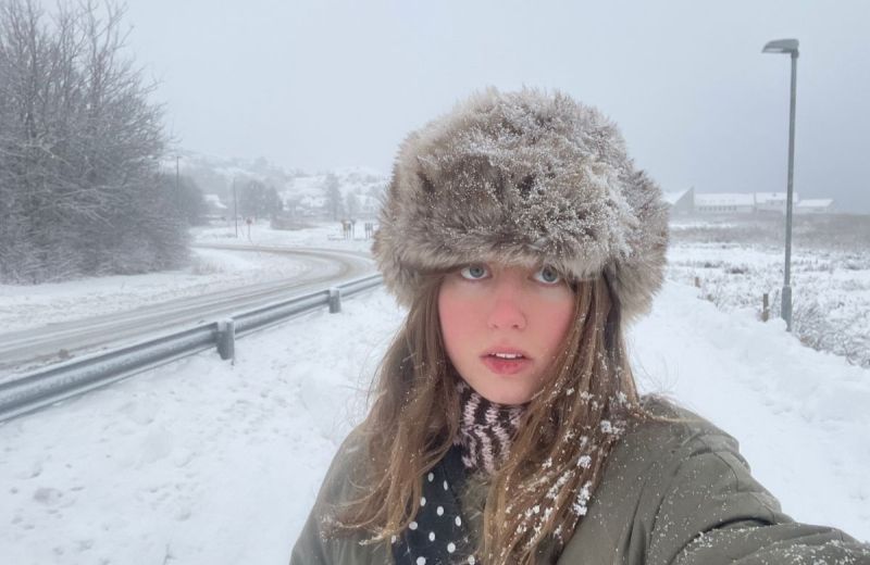 En selfie på poeten Alma Nyström Larsson iförd en fluffig mössa i snöig miljö, med en väg som går bredvid.