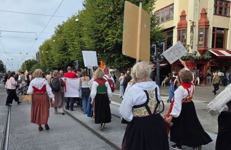 Människor i folkdräkter demonstrerar på en öppen gata med skyltar i händerna.